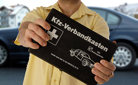 Ein Mann hält einen schwarzen Kfz-Verbandkasten in den Händen