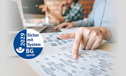 Ein Mann sitzt am Schreibtisch und zeigt auf ein Blatt Papier mit einem Diagramm, daneben das AMS-Gütesiegel.