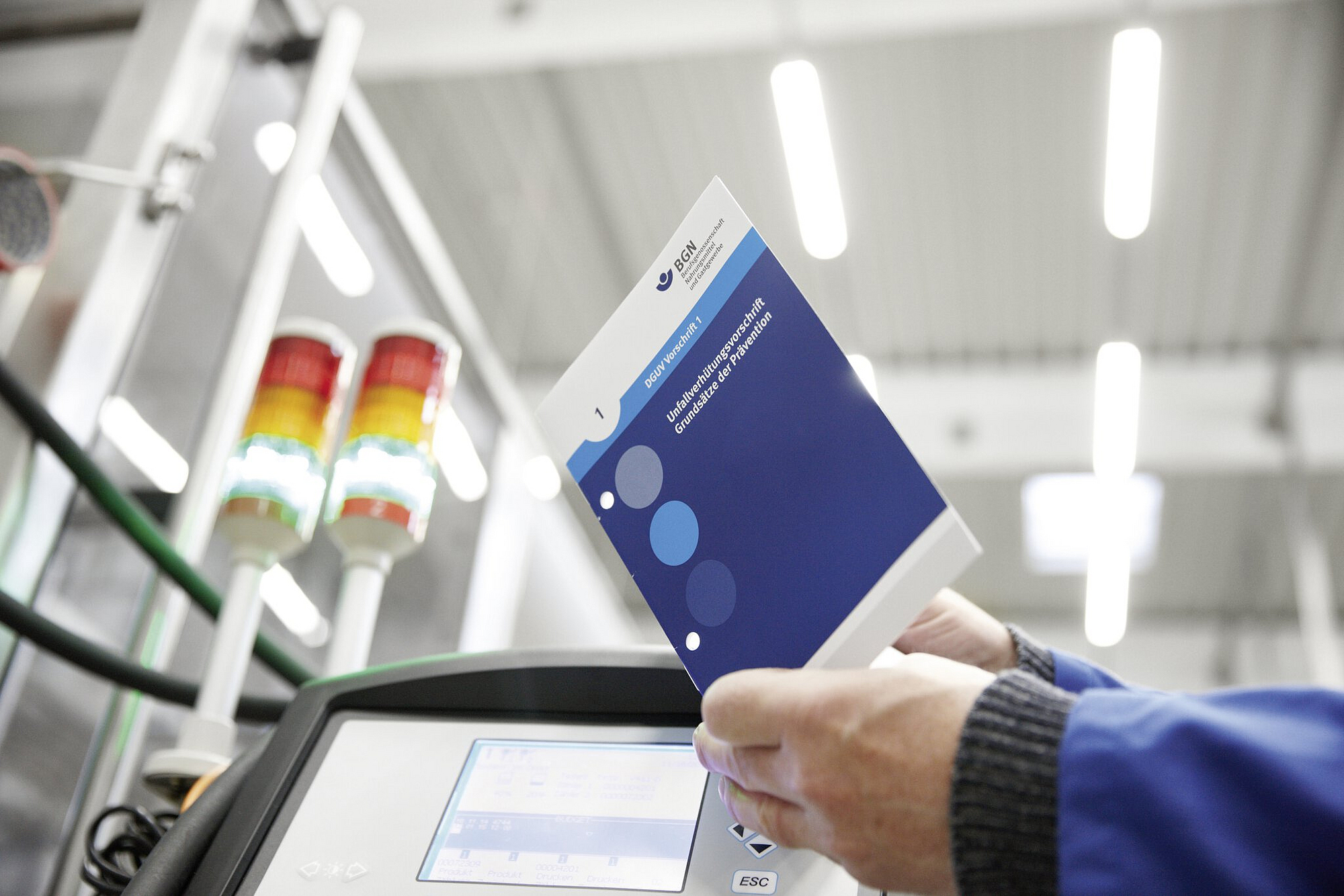 Mann hält Vorschrift in der Hand, im Hintergrund Produktionshalle