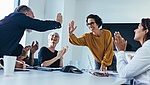 Mitarbeitende sitzen am Tisch und applaudieren, ein Mitarbeiter klatscht eine Mitarbeitende ab.