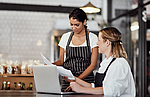 In einem Restaurant besprechen sich zwei Mitarbeiterinnen mit Papieren und einem Laptop.