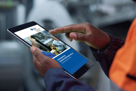  Ein Mann in Arbeitskleidung hält in einer Produktionsanlage ein Tablet in der Hand